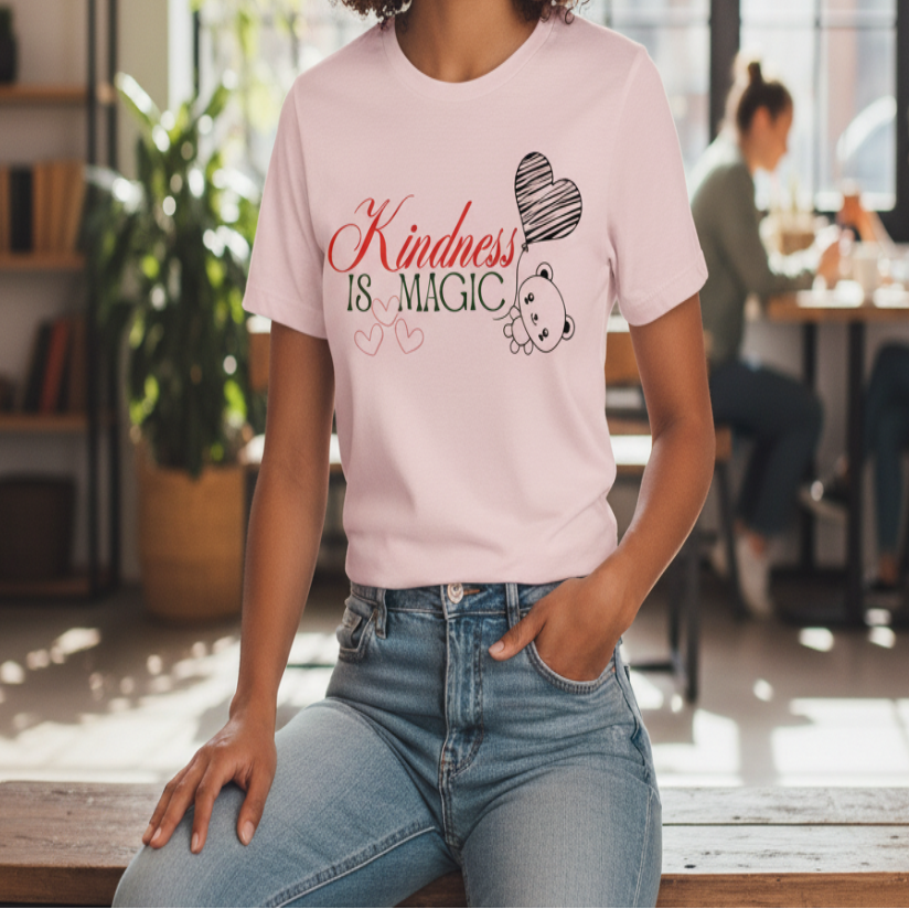 Woman wearing a pink t-shirt with 'Kindness is Magic' text sitting on a bench in a bright room.